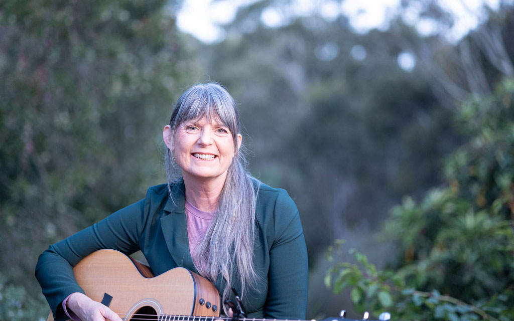 Josephine Mary Schmidt, singer-songwriter and producer of many Christian albums, is holding her guitar, smiling in the joy of her testimony and Salvation in Christ Jesus.