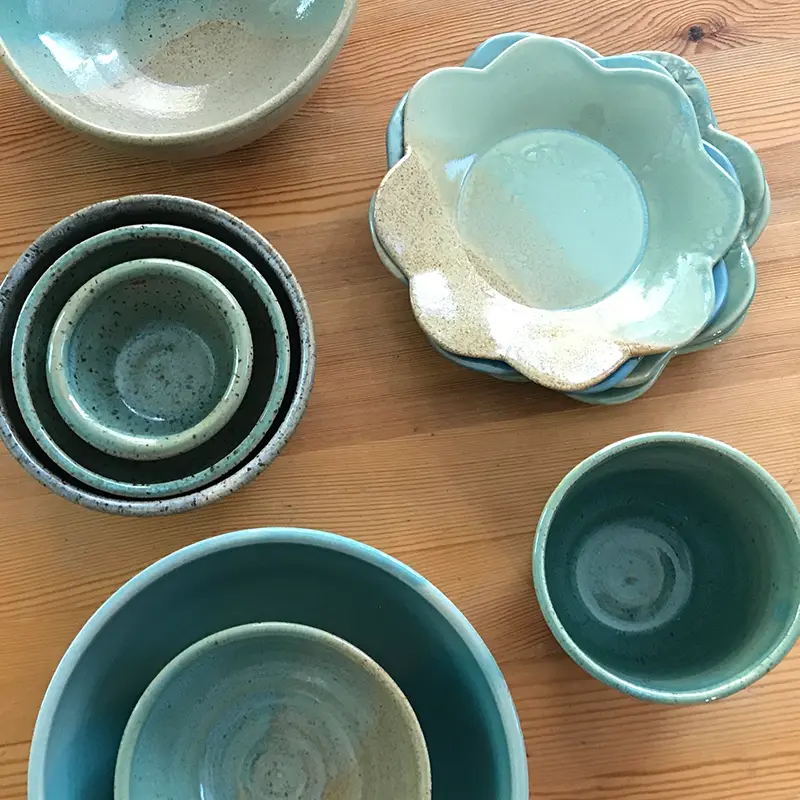 An overhead view of a group of aqua blue and tan pottery bowls and small plates stacked on a tabletop.