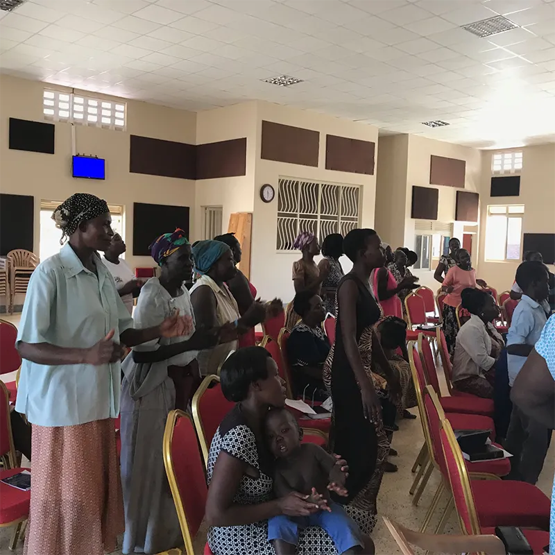 Women from Soroti, Uganda, standing and sitting, smiling and clapping, joyful in worship.